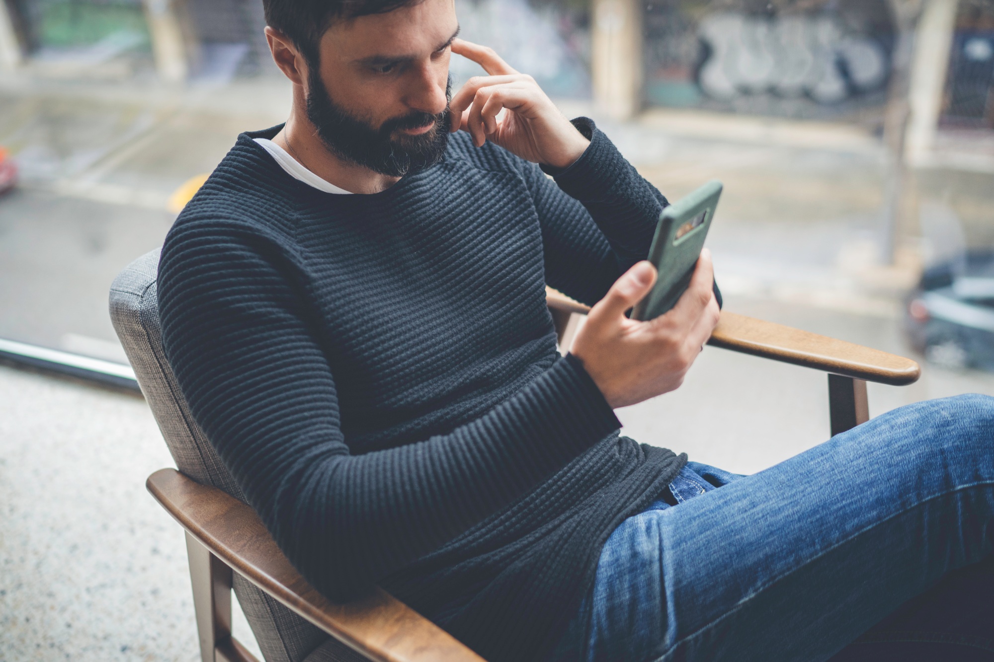 Cheerful caucasian man in black pullover using mobile phone application for mobile blogging.