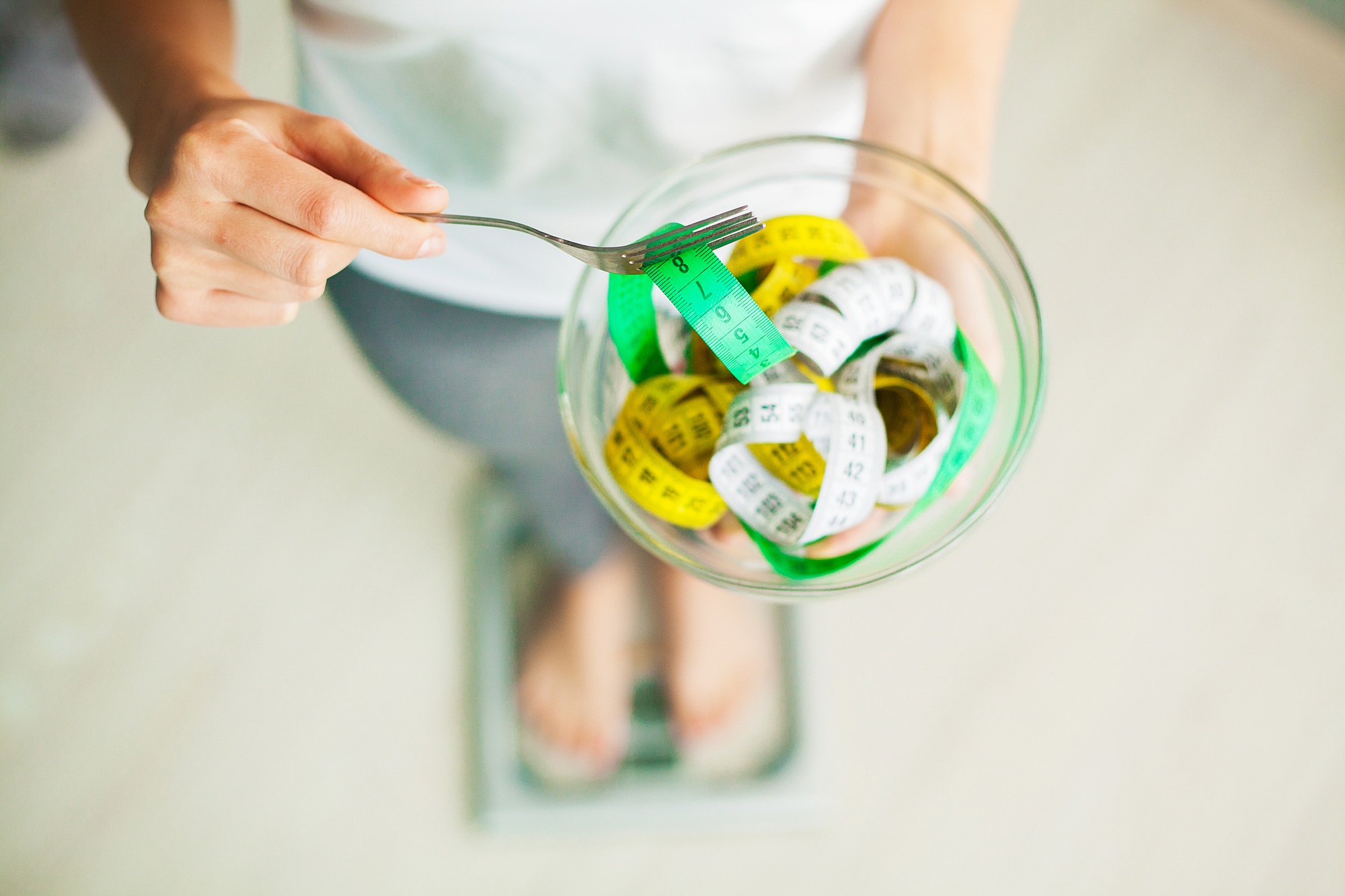 Diet and Weight Loss. Woman holds bowl and fork with measuring tape